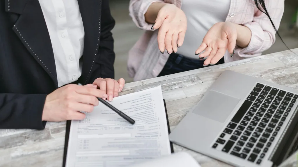 Therapist and client discussing insurance paperwork with laptop and forms on the table