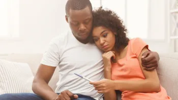 Couple sitting on a couch holding a pregnancy test, supporting each other through infertility struggles