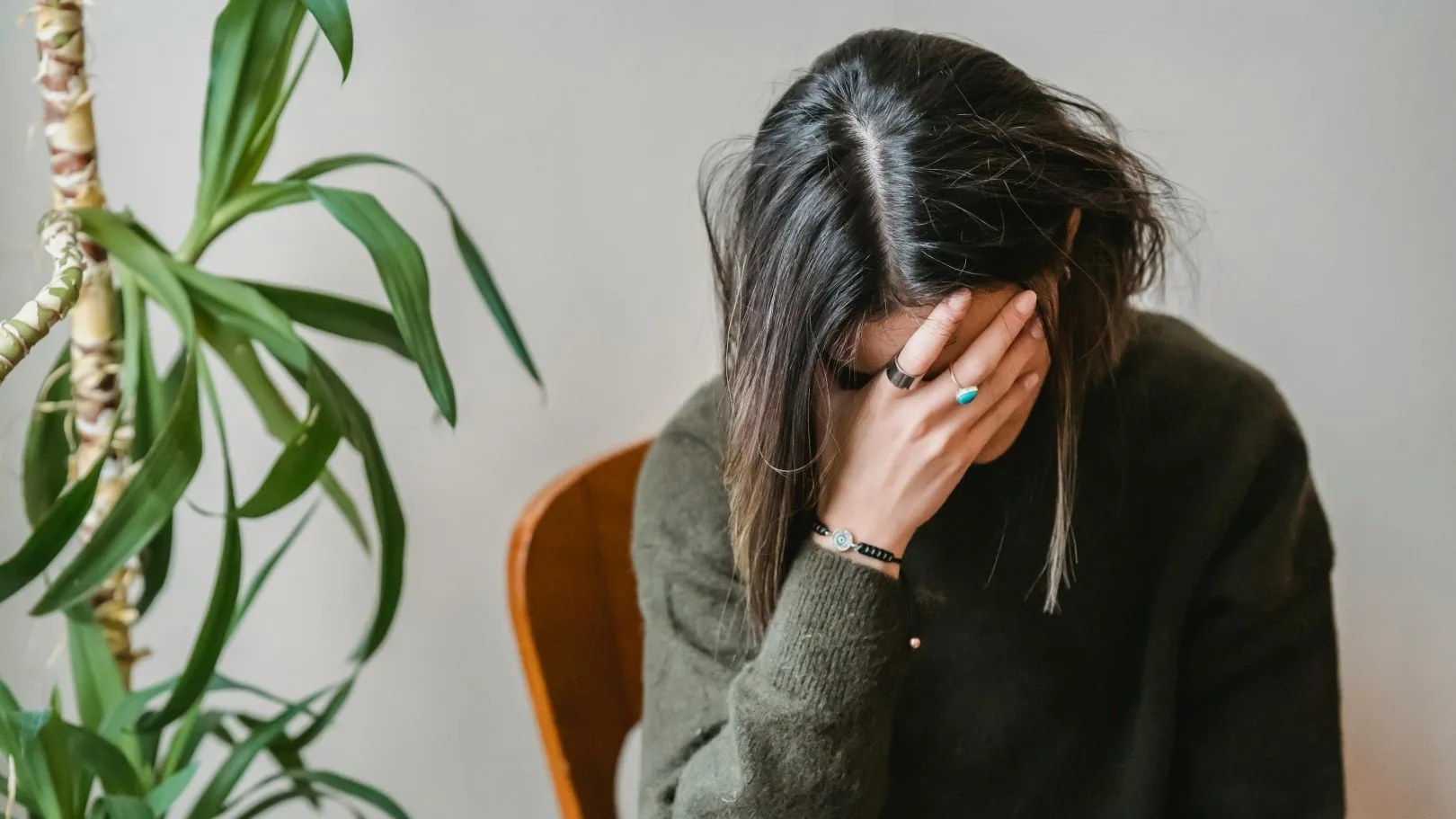Woman overwhelmed with anxiety, head in hand, seated next to a plant in a therapy setting