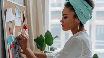 Neurodivergent woman thoughtfully adding notes to a vision board near a window with houseplants
