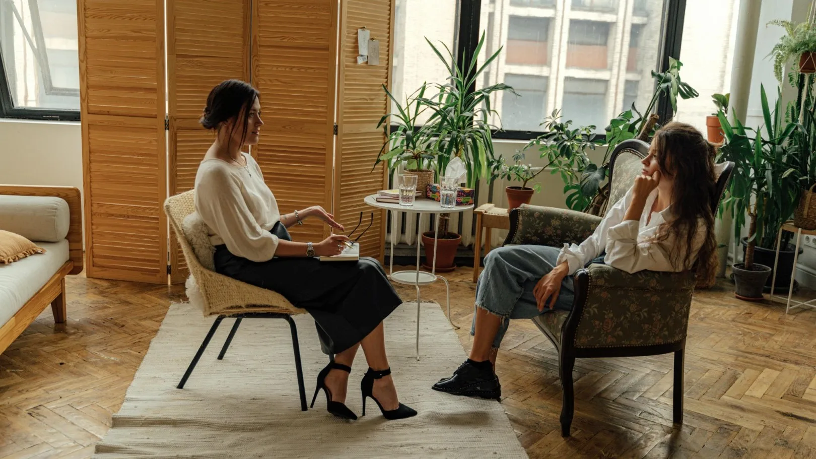 Therapist and client talking in a calm, trauma-informed therapy session surrounded by plants