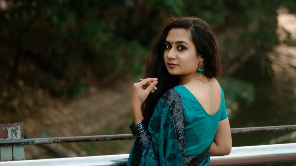 Woman in teal sari looking back over her shoulder near water, symbolizing reflection and emotional healing