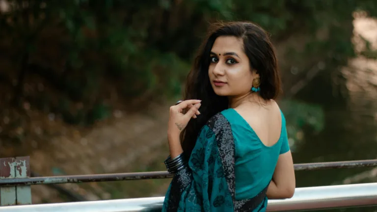 Woman in teal sari looking back over her shoulder near water, symbolizing reflection and emotional healing