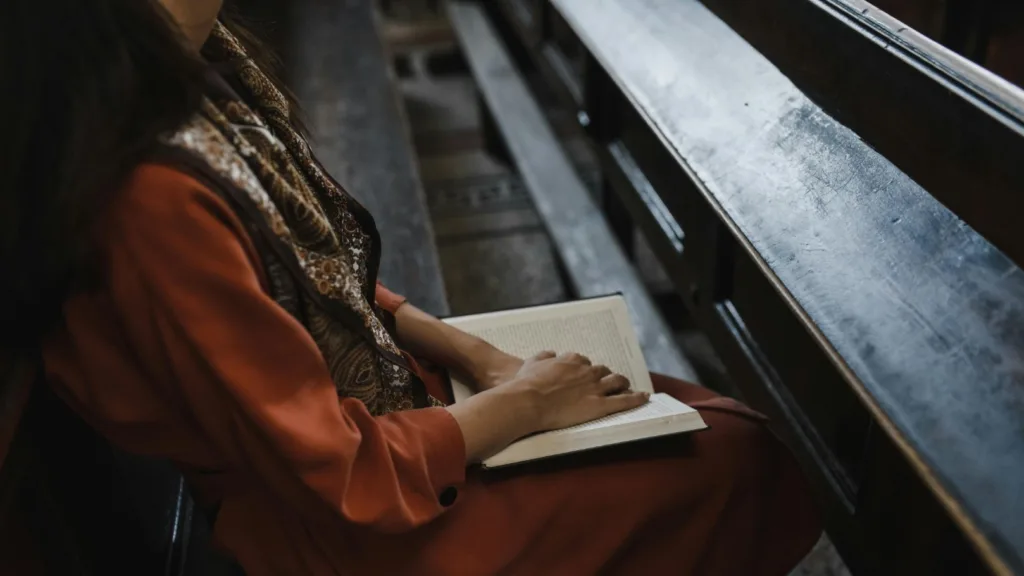Person sitting in a wooden pew with an open book, symbolizing quiet reflection or spiritual healing.