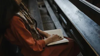 Person sitting in a wooden pew with an open book, symbolizing quiet reflection or spiritual healing.