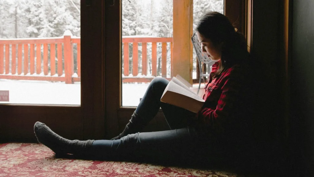 Highly sensitive woman reading by a window during winter, taking quiet time for emotional regulation
