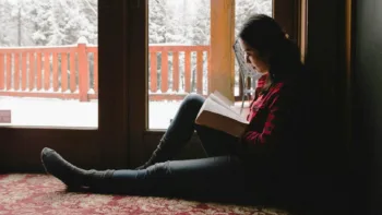 Highly sensitive woman reading by a window during winter, taking quiet time for emotional regulation
