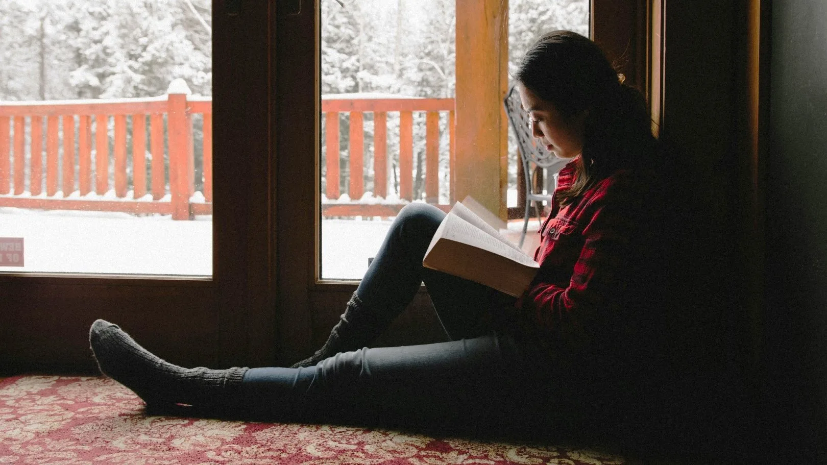 Highly sensitive woman reading by a window during winter, taking quiet time for emotional regulation
