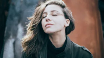 Woman practicing mindfulness with eyes closed and peaceful expression, outdoors in cool weather