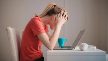Woman sitting at desk with head in hands, looking overwhelmed in front of a laptop