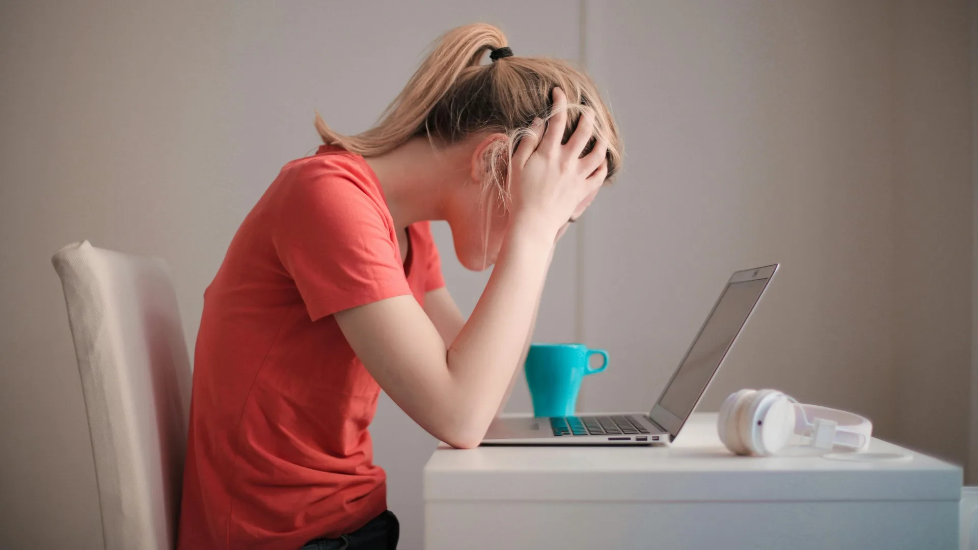 Woman sitting at desk with head in hands, looking overwhelmed in front of a laptop