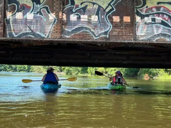 Therapist Irene Ivanac kayaking under a graffiti-covered bridge on a calm river