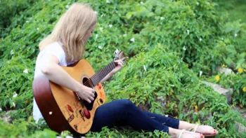Therapist Megan Fordon sitting outdoors playing guitar, surrounded by greenery
