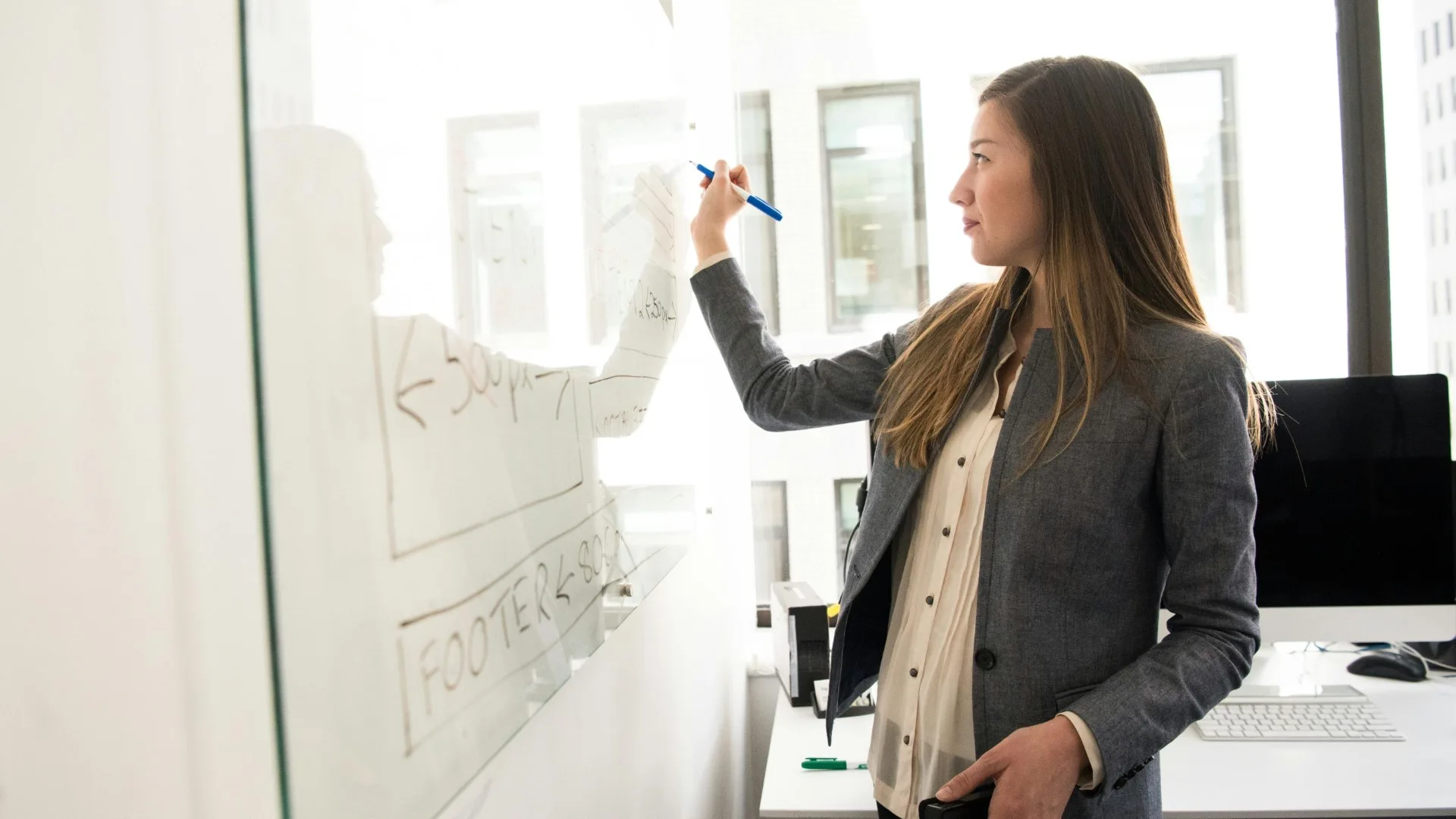 Female educator writing on a whiteboard in a bright classroom, symbolizing the professional and personal mental health journey of public school teachers