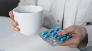 A person holding a cup and a blister pack of blue capsules, representing mental health medication.