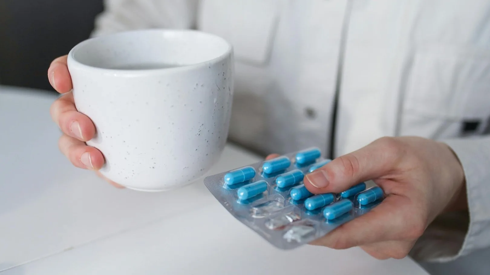 A person holding a cup and a blister pack of blue capsules, representing mental health medication.