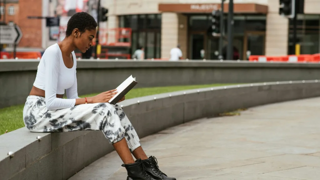 Young woman reading outside on a stone wall, symbolizing how nervous system regulation supports trauma healing and growth