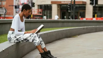 Young woman reading outside on a stone wall, symbolizing how nervous system regulation supports trauma healing and growth