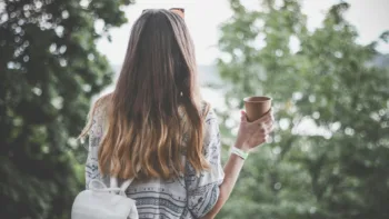 Woman holding a coffee mug outdoors, seen from behind, representing a peaceful moment during her anxiety healing journey