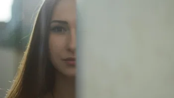 Close-up of a woman with half her face hidden behind a wall, symbolizing trauma, introspection, or emotional division.