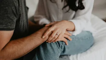 Close-up of a couple holding hands on a bed, symbolizing emotional closeness and relational entanglement often seen in codependent relationships