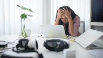 Woman sitting at a cluttered desk, holding her head in distress, representing the feeling of being trapped in an anxiety spiral
