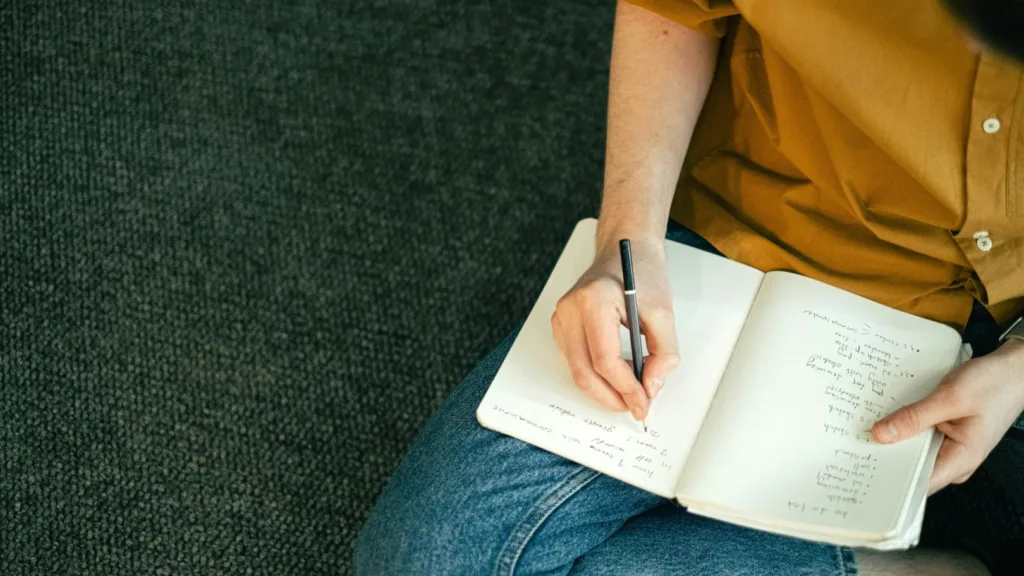 Person sitting cross-legged and writing in a journal, representing reflection and preparation for EMDR therapy.