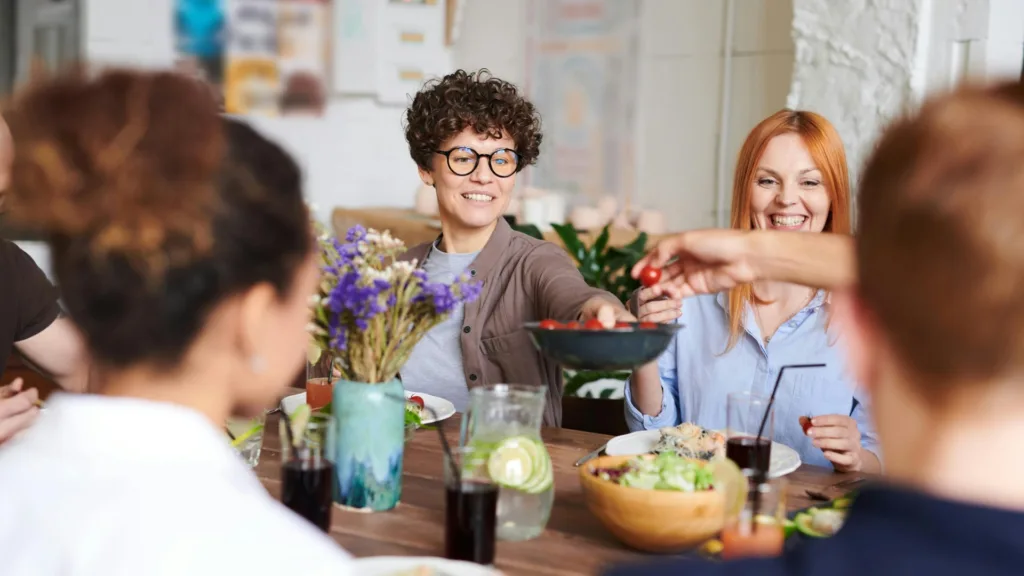 Group of people enjoying a shared meal, laughing and passing food around a table in a relaxed setting