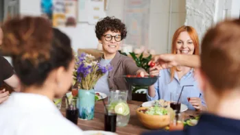 Group of people enjoying a shared meal, laughing and passing food around a table in a relaxed setting