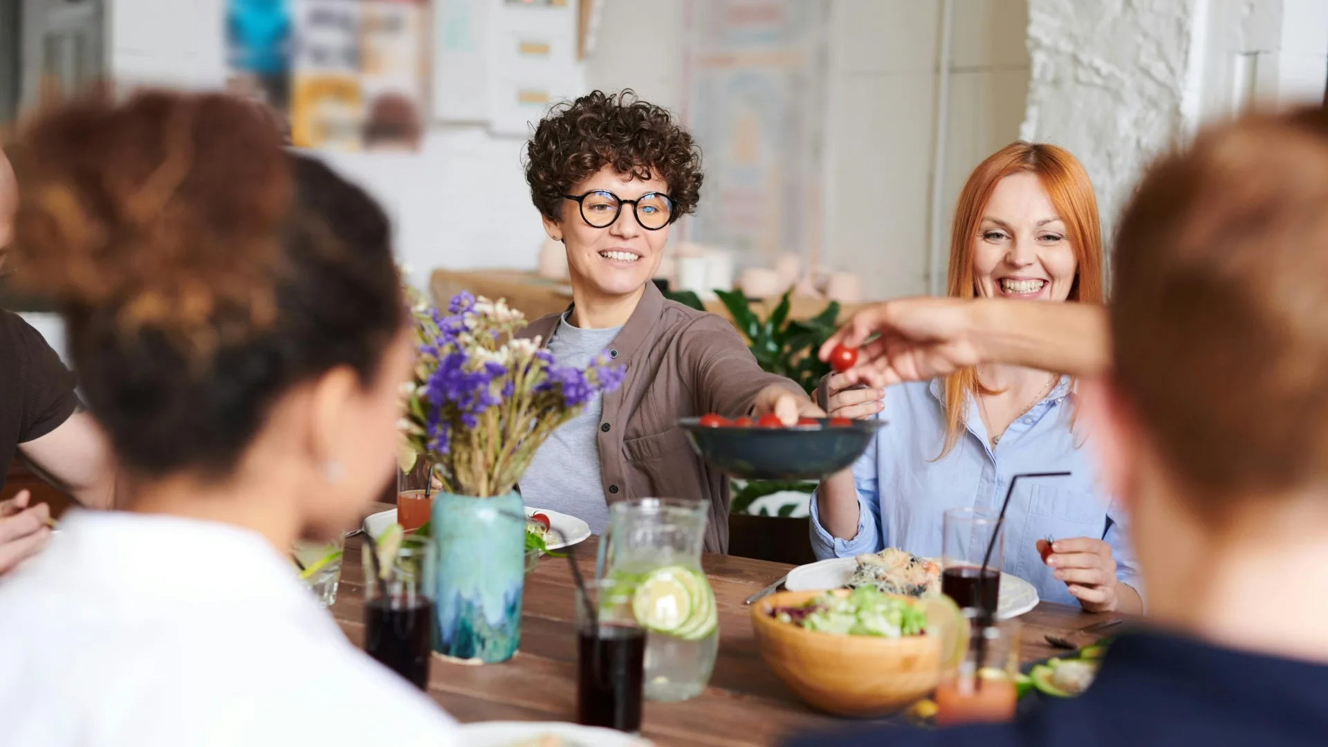 Group of people enjoying a shared meal, laughing and passing food around a table in a relaxed setting