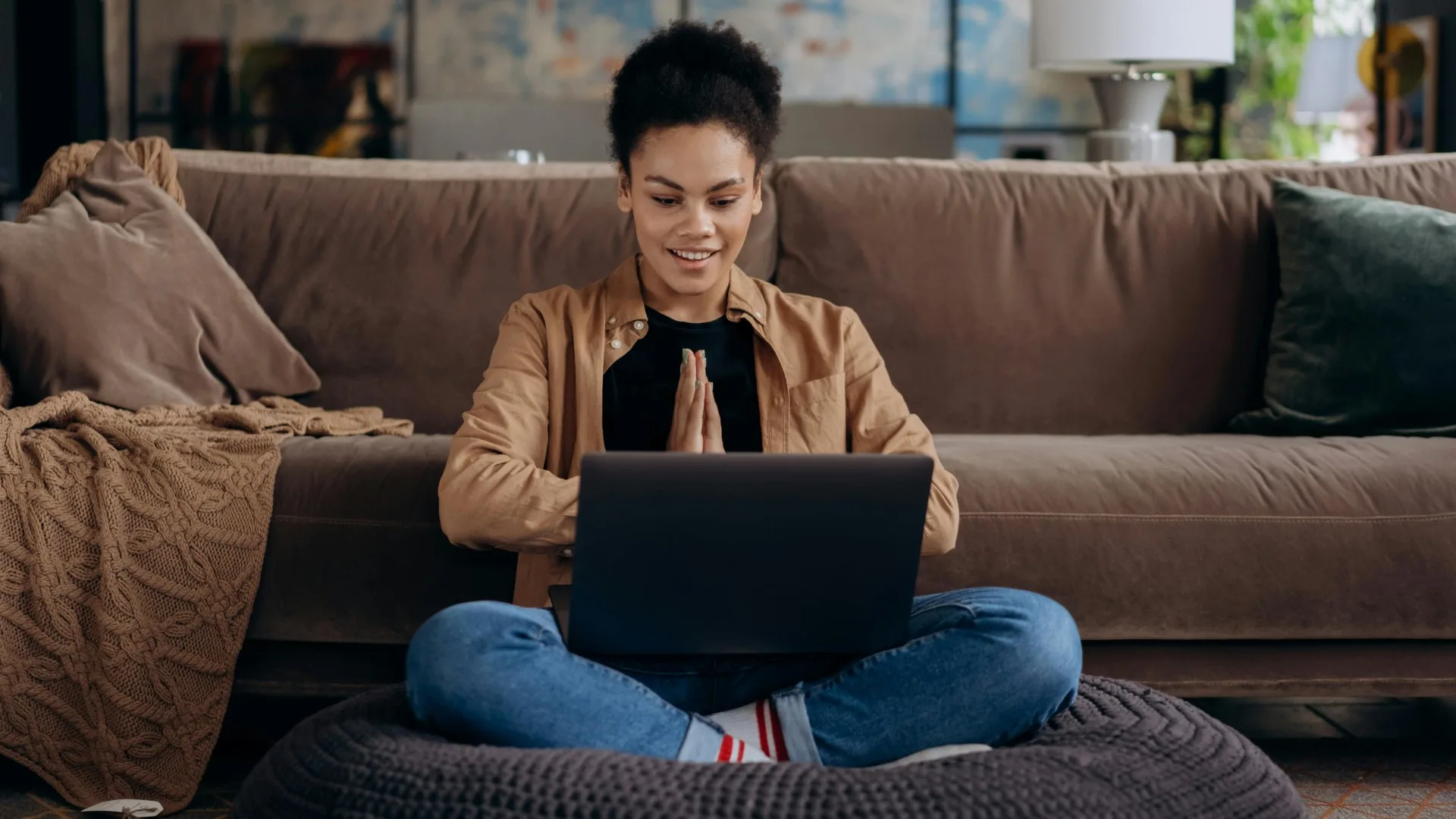 Smiling woman sitting cross-legged on the floor, engaging with a laptop in a calm and cozy home setting