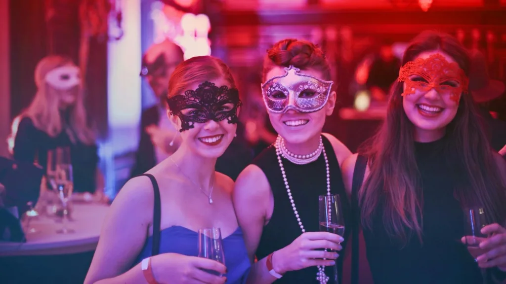 Three women wearing masquerade masks at a lively party, representing social connection and emotional boundaries