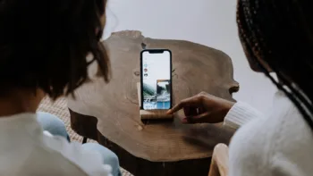 Two people looking at a smartphone on a table, with one pointing at social media content on the screen.