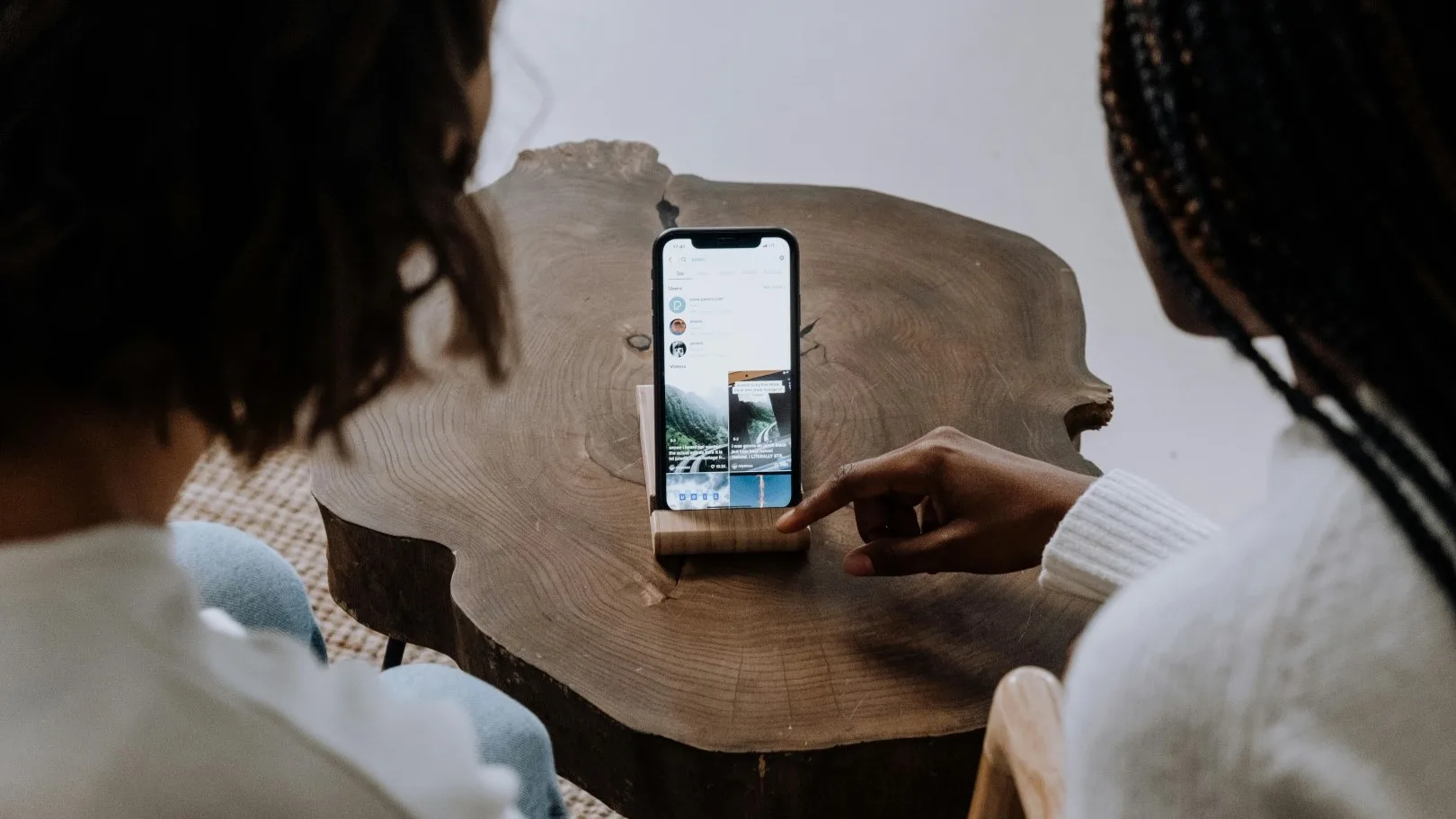 Two people looking at a smartphone on a table, with one pointing at social media content on the screen.