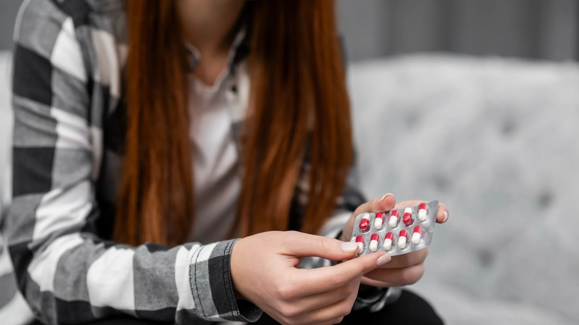 Person holding blister pack of anxiety medication while seated on a couch