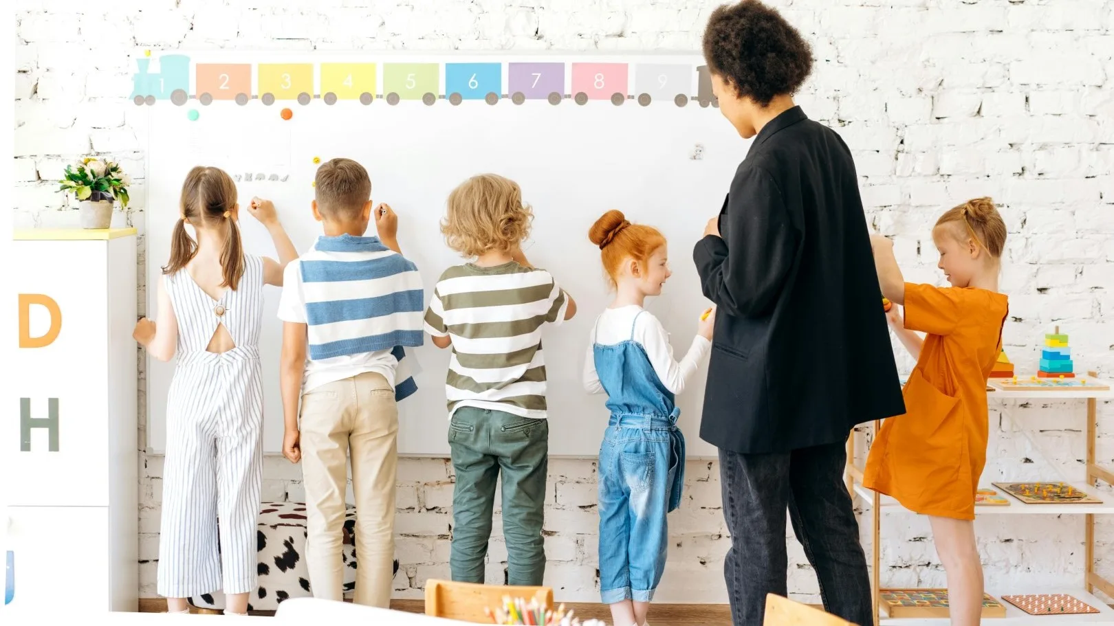 Teacher standing with a group of young children at a classroom whiteboard during an activity