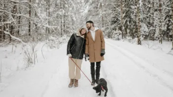Couple walking a dog in the snow, leaning on each other and enjoying a calm winter moment