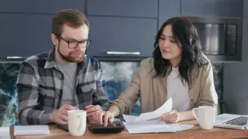 Couple reviewing finances together at home with a calculator and paperwork