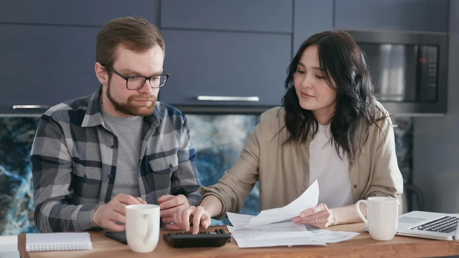 Couple reviewing finances together at home with a calculator and paperwork