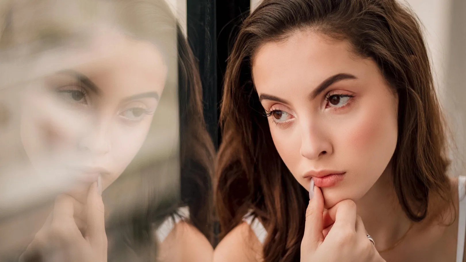 Young woman staring at her reflection with a pensive expression, symbolizing stress or self-reflection.