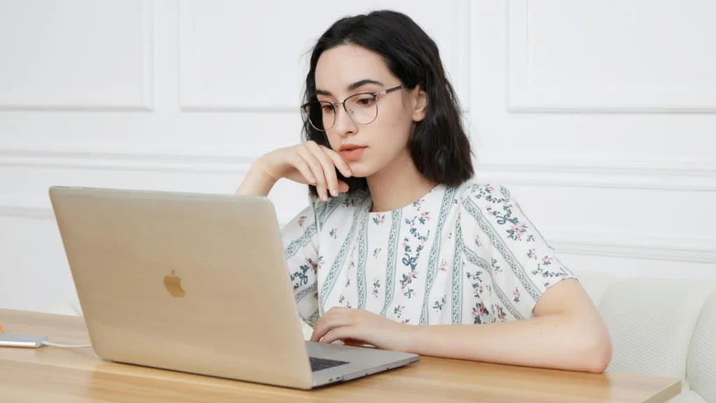 Young woman wearing glasses looking at a laptop, representing virtual EMDR therapy or telehealth counseling.