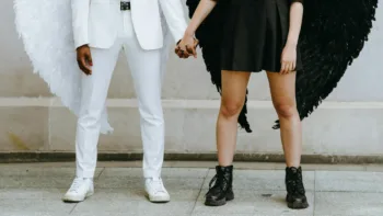 Two people holding hands, one dressed in white with white angel wings, the other in black with black wings, symbolizing emotional duality
