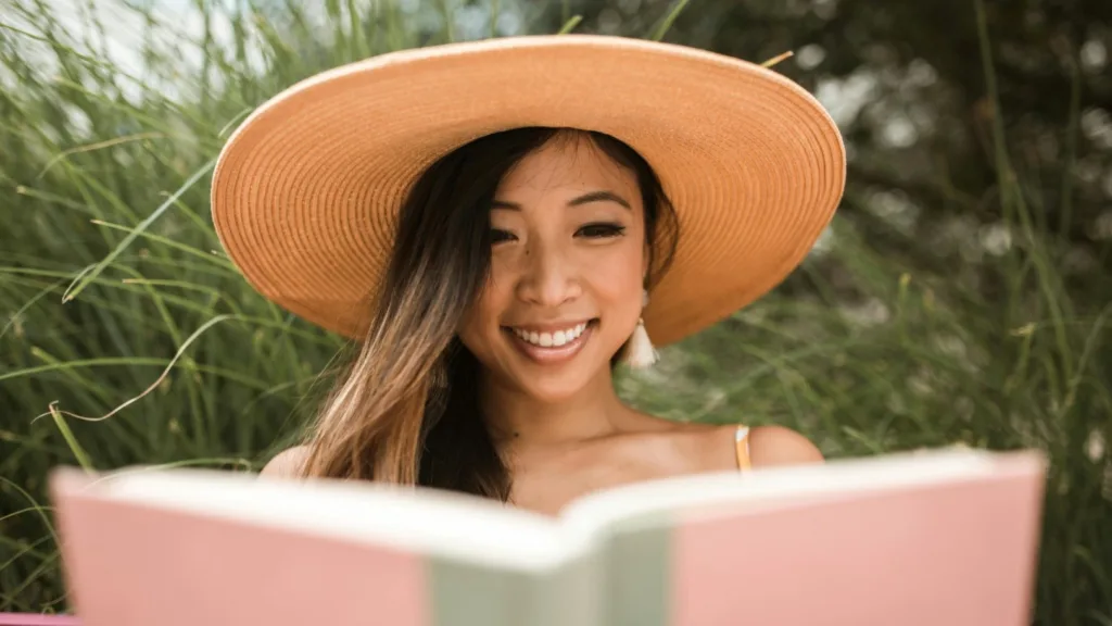 Smiling woman reading a book outdoors, practicing self-care and emotional wellbeing