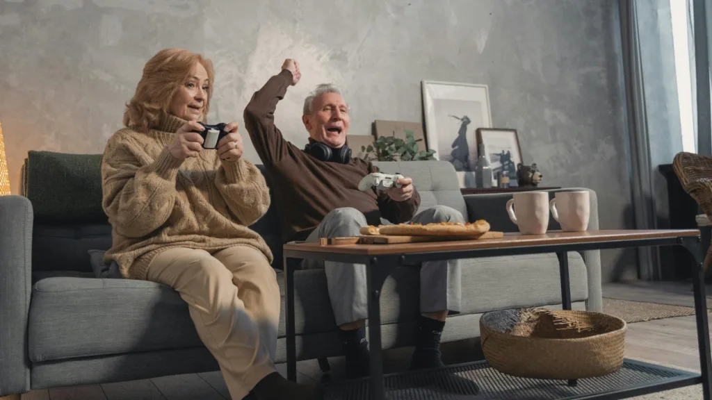 Older couple enthusiastically playing video games on the couch, representing emotionally immature parent dynamics