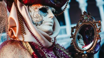 Person in ornate Venetian mask holding mirror, symbolizing identity and masking in the neurodivergent experience