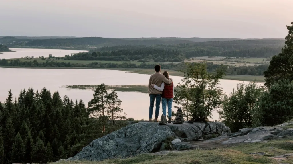 Couple standing on cliffside overlooking scenic lake and forest, symbolizing connection and emotional healing
