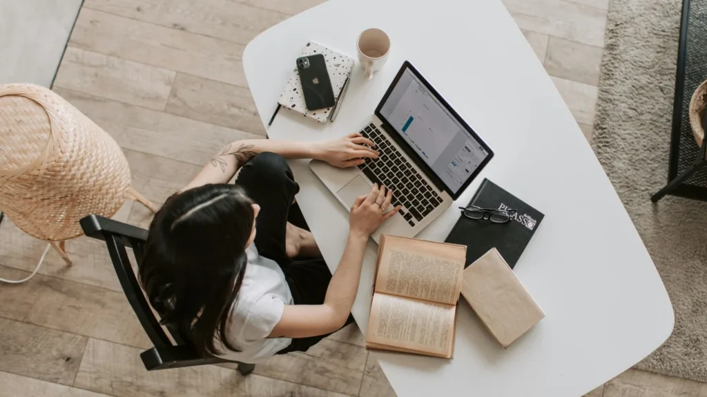 Woman researching mental health resources on laptop with books and coffee on desk