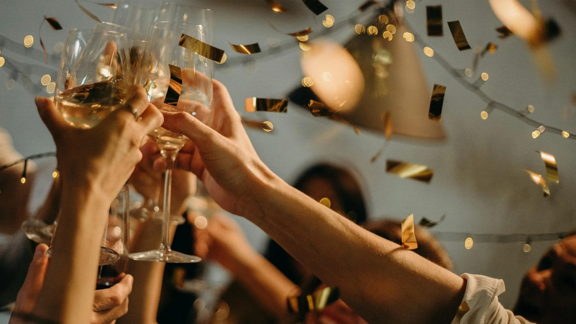 People clinking champagne glasses at a New Year’s celebration with gold confetti falling