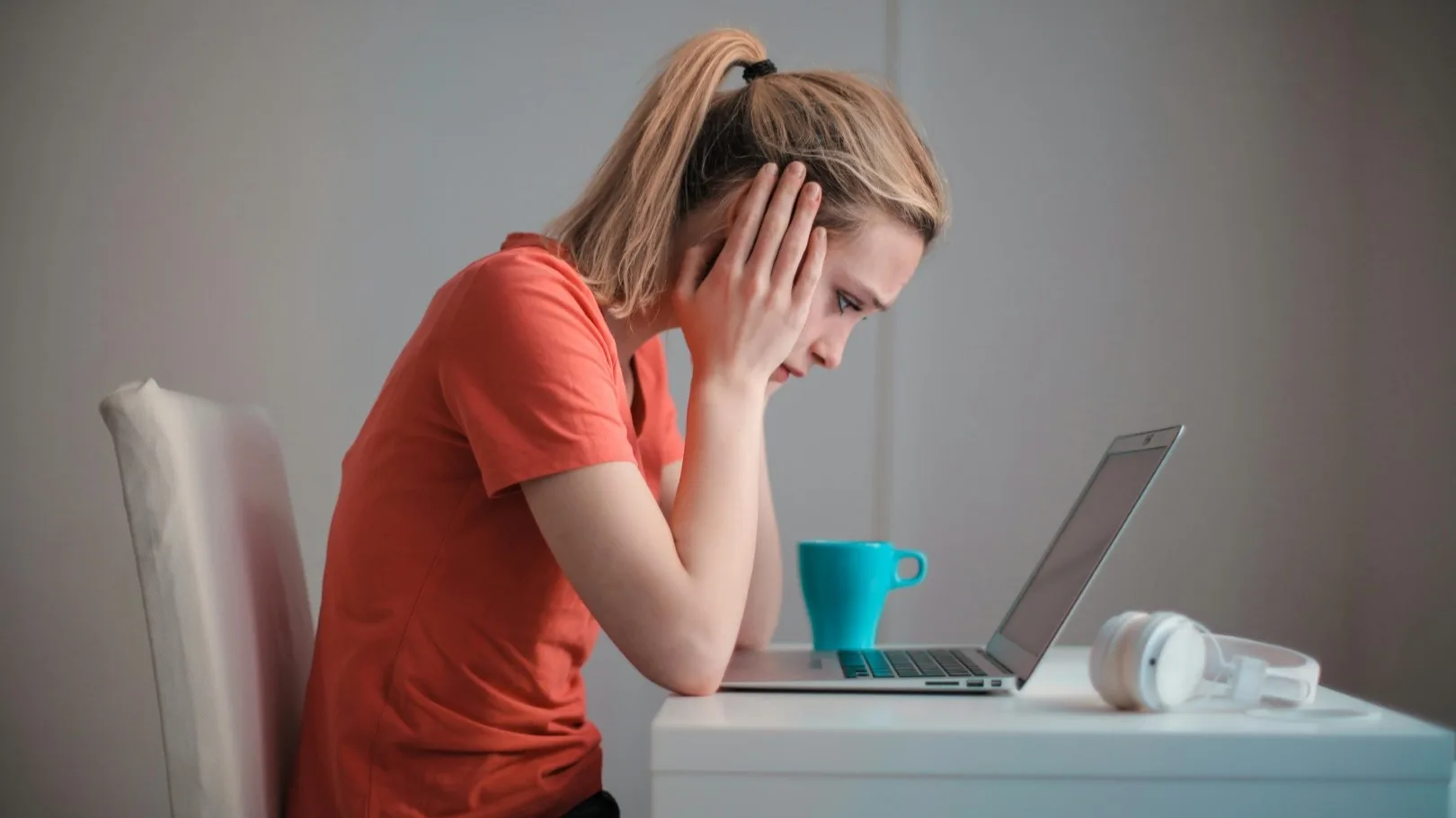 Stressed woman with head in hands staring at laptop, feeling overwhelmed while researching therapy options