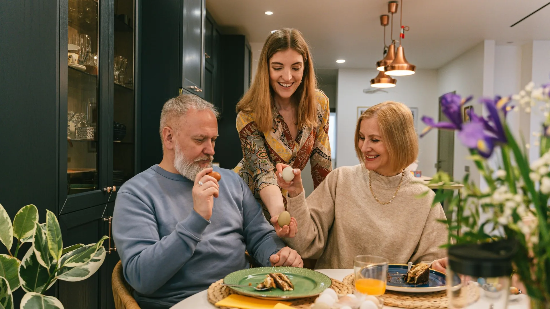 Adult daughter sitting with her parents at a kitchen table, sharing a warm conversation over breakfast